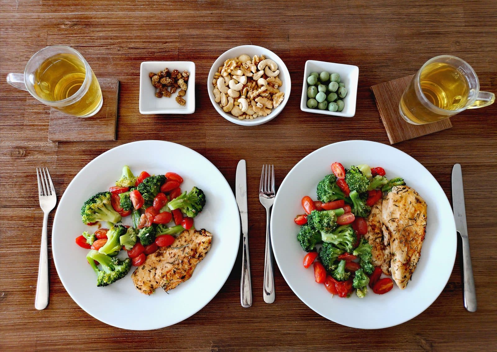 Mesa de madeira com pratos equilibrados de frango, legumes, castanhas e chá