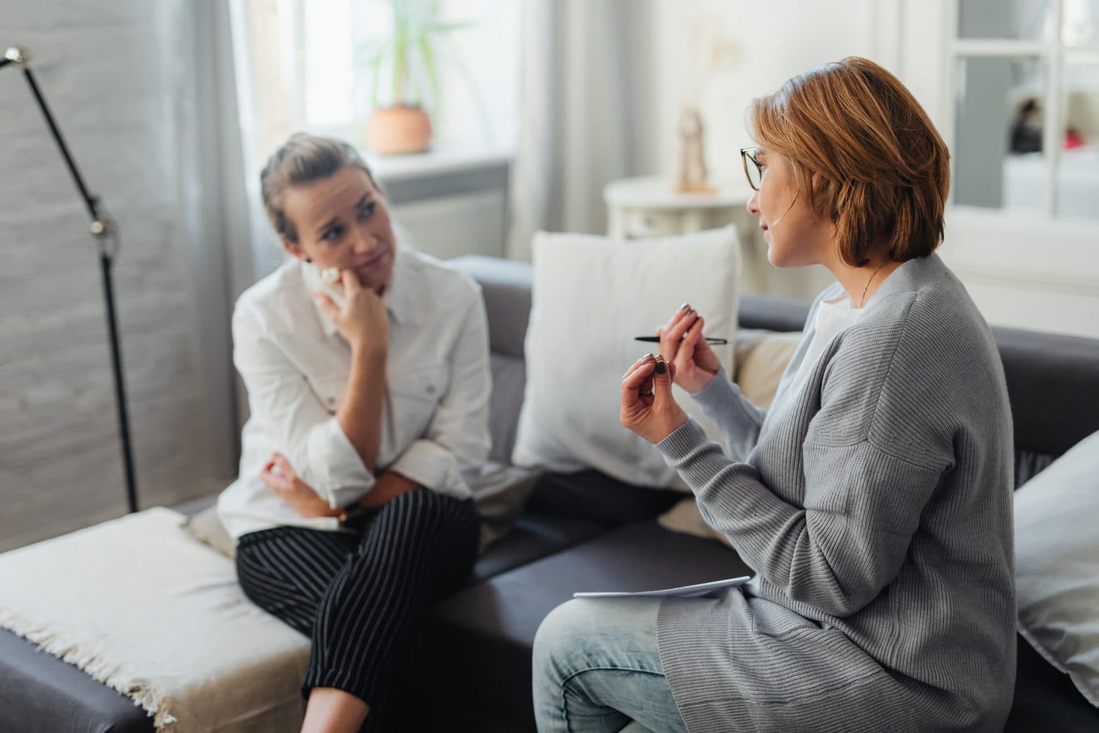 Duas mulheres conversam com atenção sentadas em sofás sob luz natural
